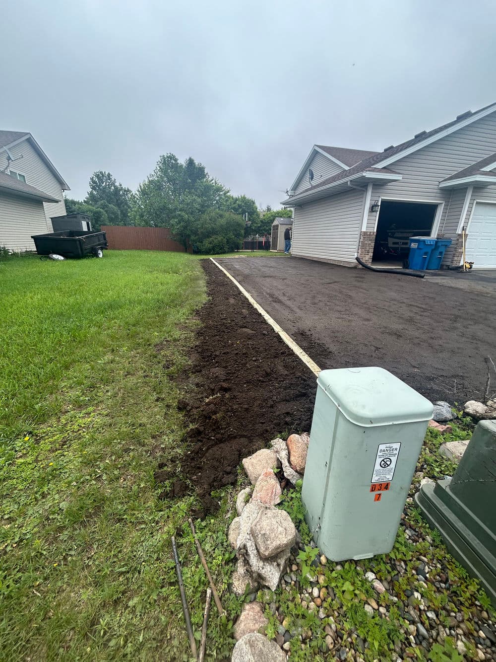 Freshly tilled earth alongside a residential driveway with grass on one side and utility box.