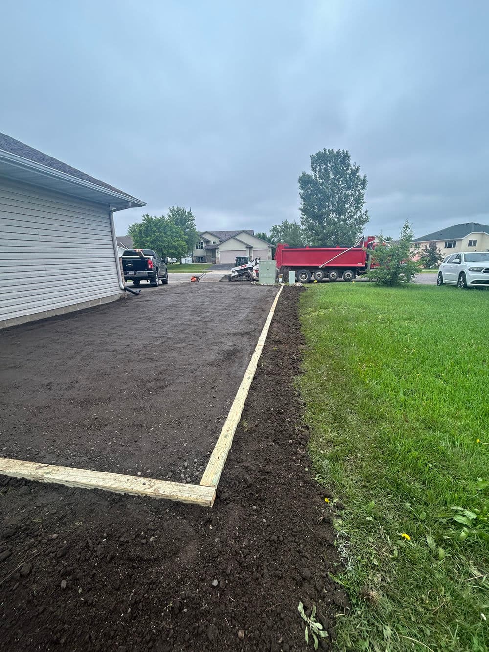 Newly prepared gravel driveway next to a home, with landscaping materials and vehicles nearby.