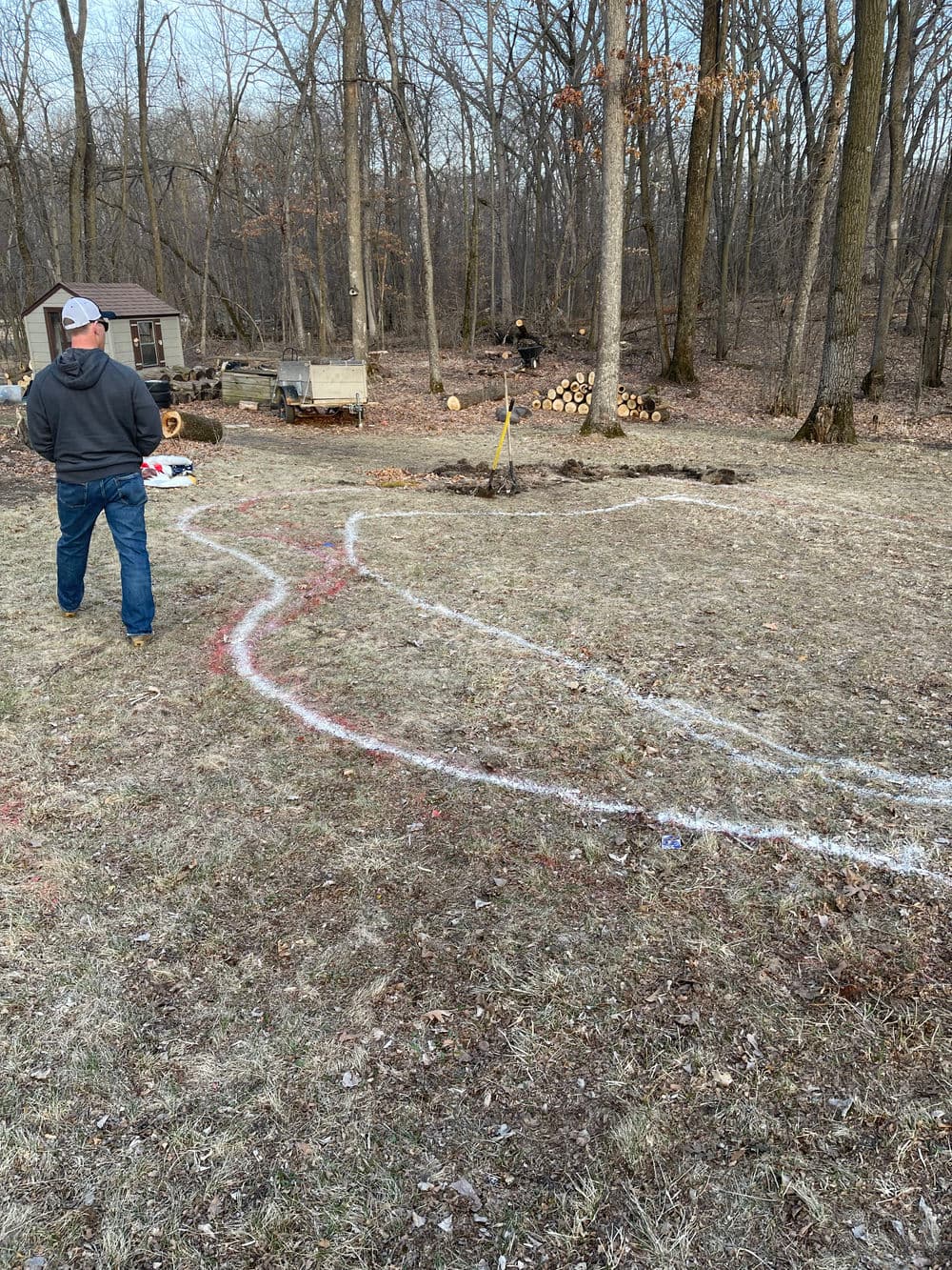 Man marking a landscaping design in a wooded backyard with white chalk outline.