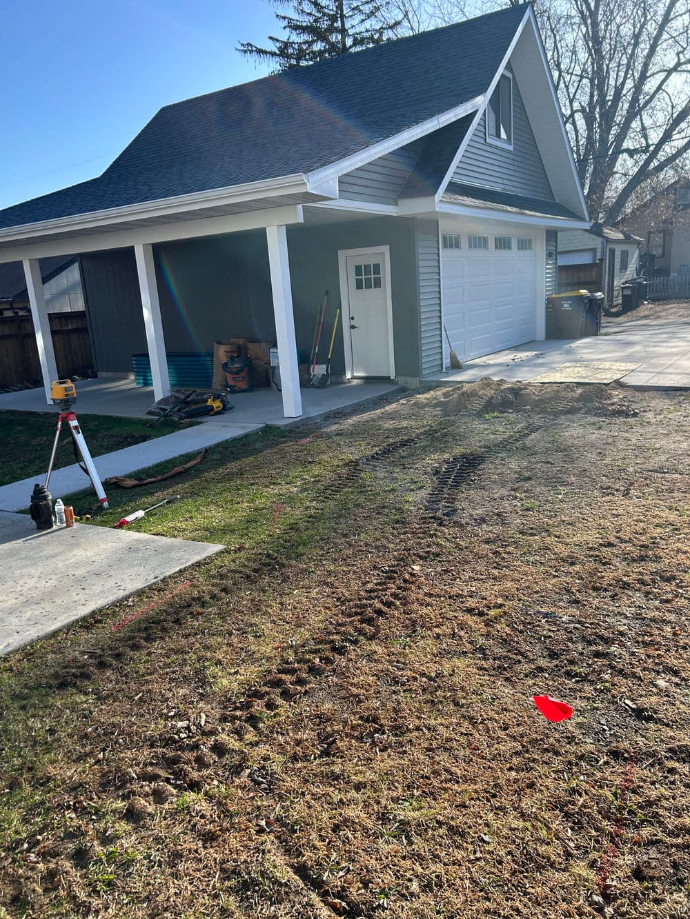Newly constructed garage with driveway, landscaping marks, and construction tools nearby.