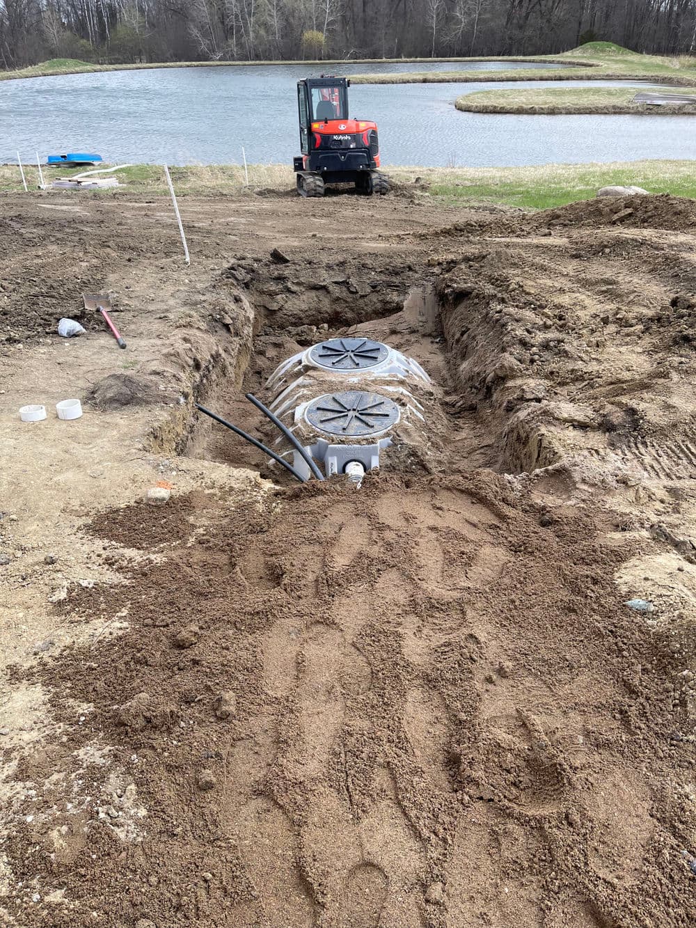 Construction site featuring a trench with two drainage tanks near a pond.