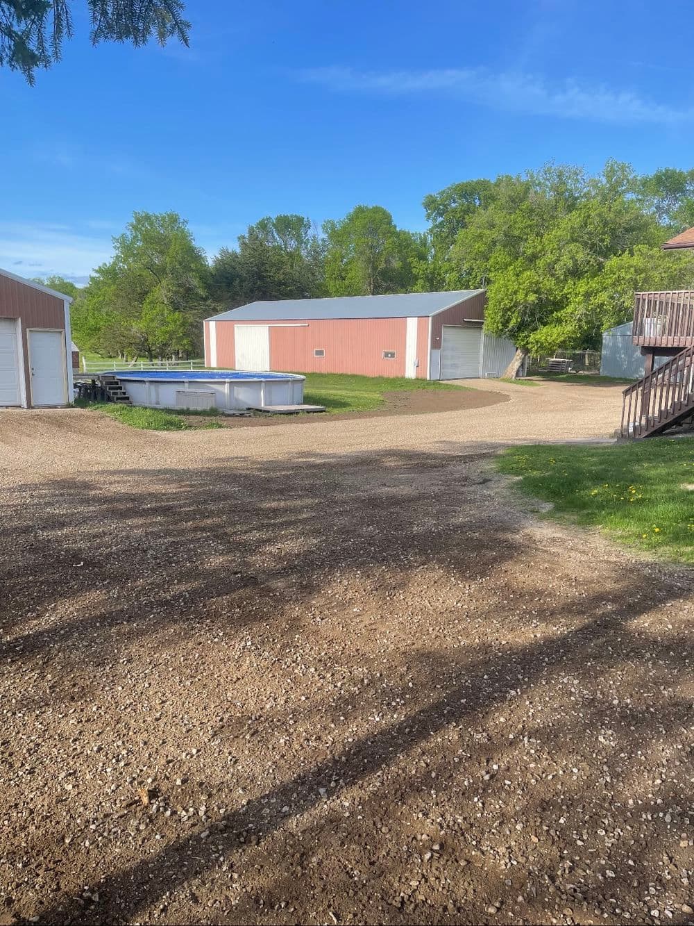 Gravel driveway leading to red barns and pool area surrounded by green trees.