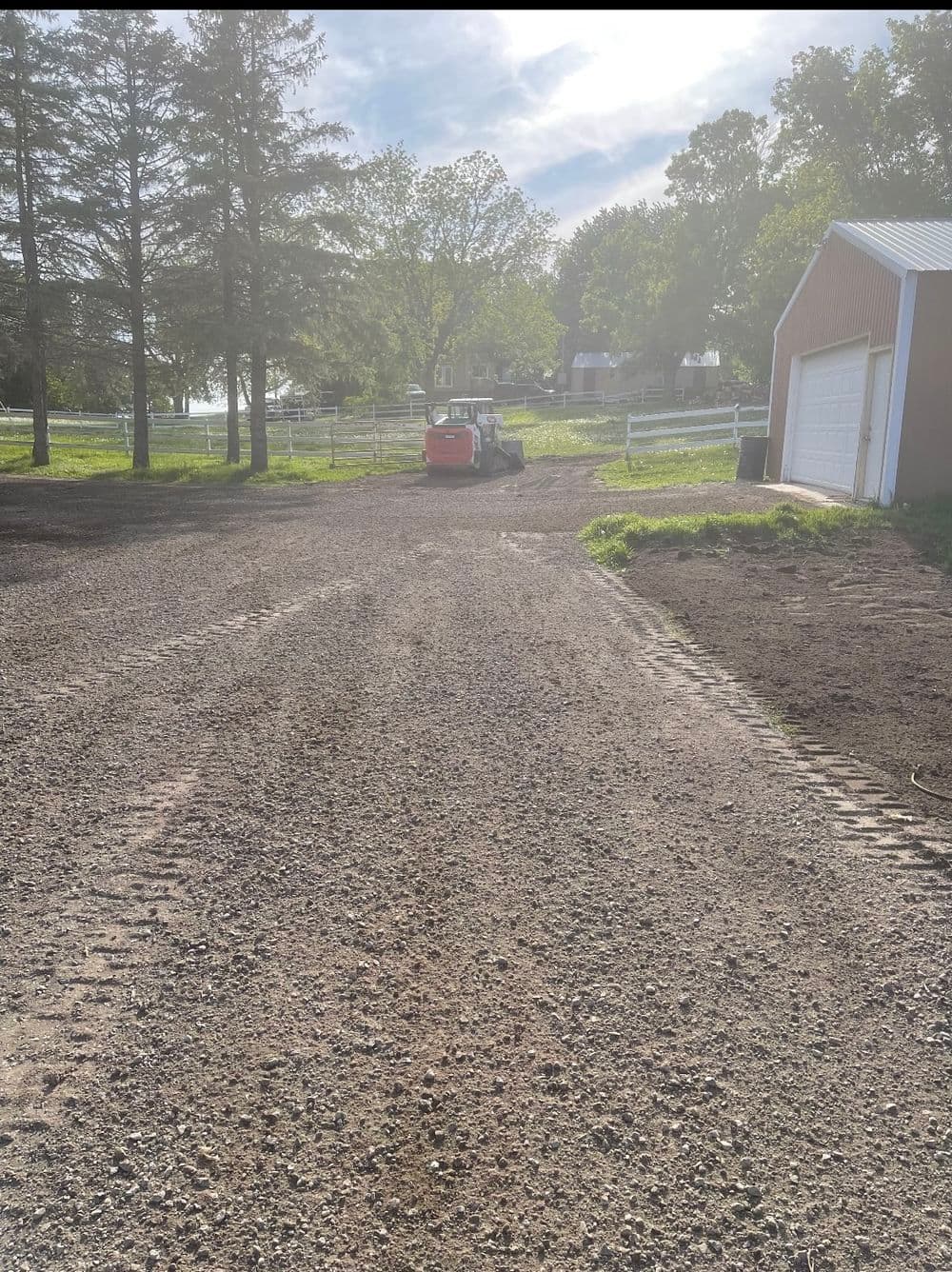 Gravel driveway leading to a barn and tractor on a sunny farm landscape.