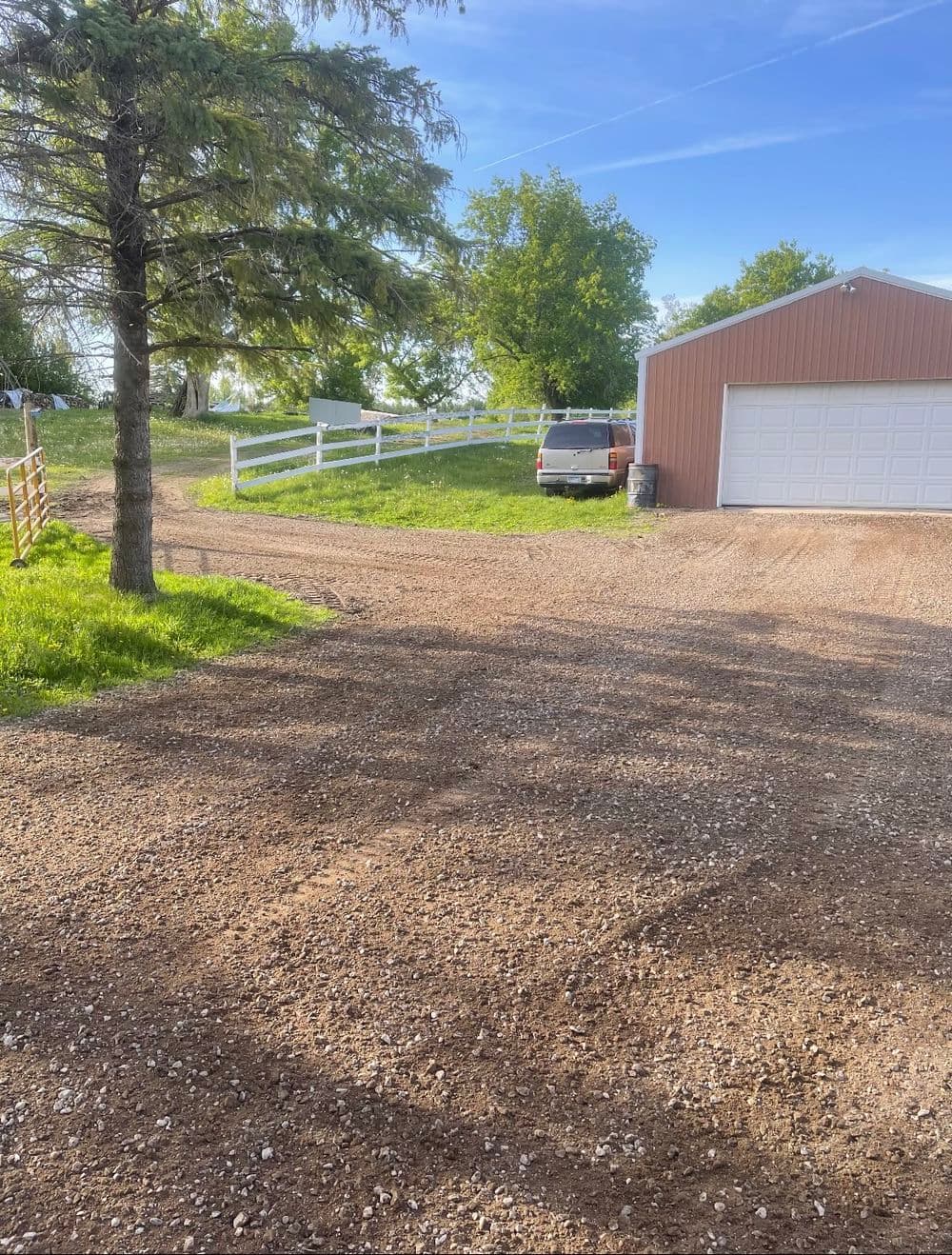 Gravel driveway leading to a barn-style garage with a parked vehicle and trees nearby.