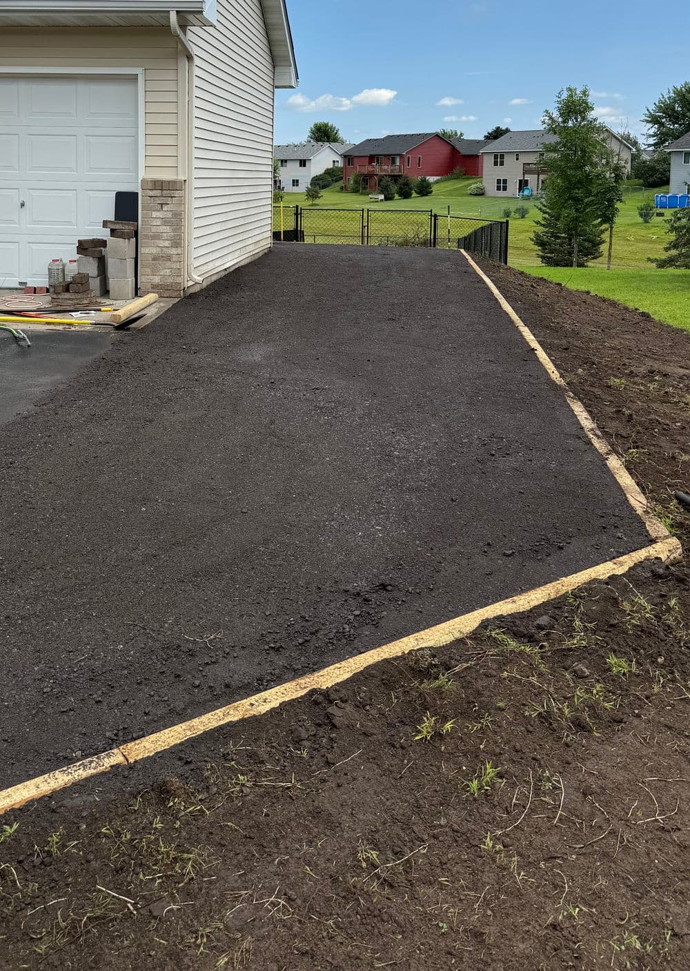 Freshly paved driveway next to a house, featuring a yellow edging and a grassy area.
