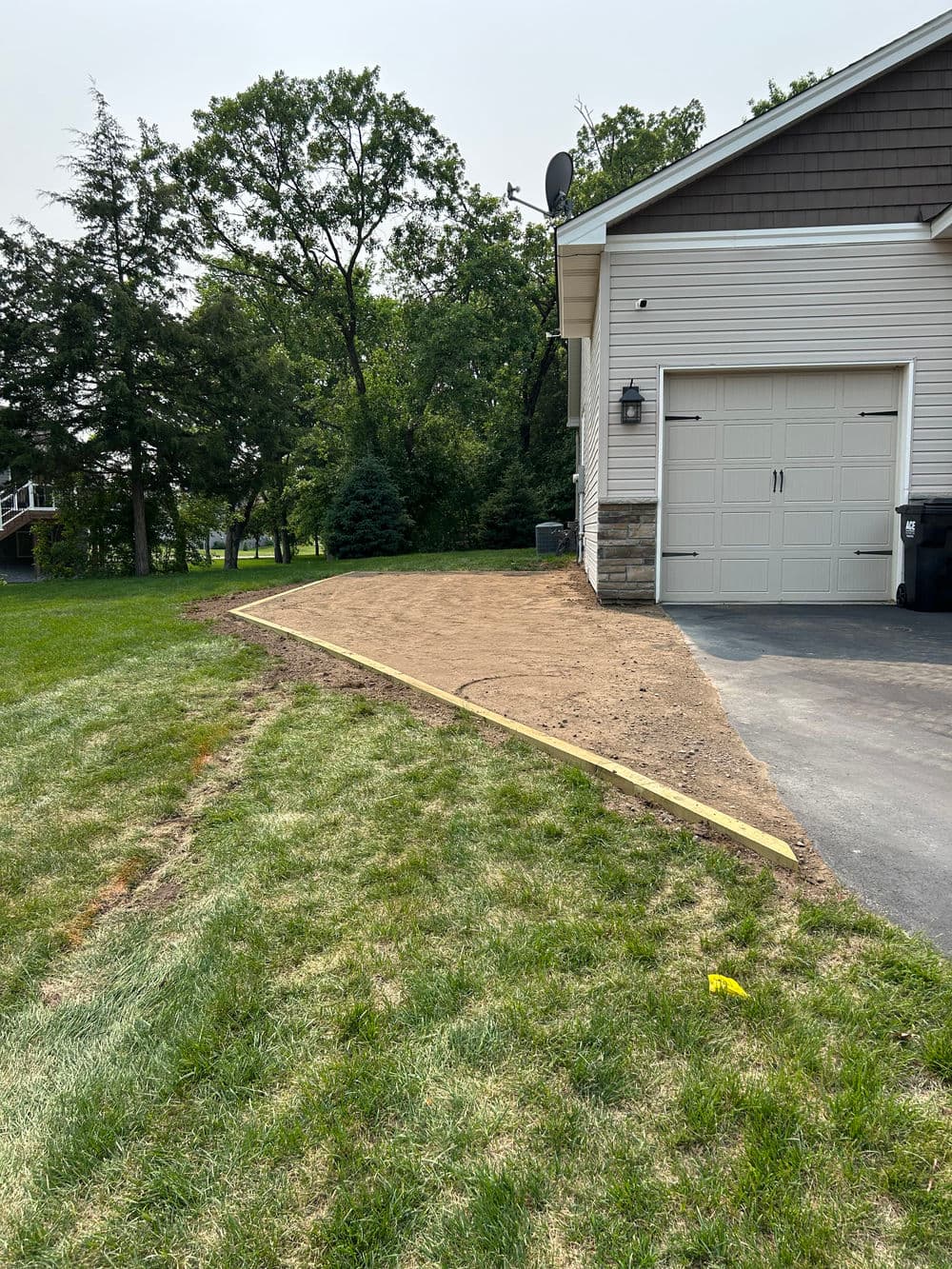 Landscape preparation with dirt and wooden edging next to a house and garage.