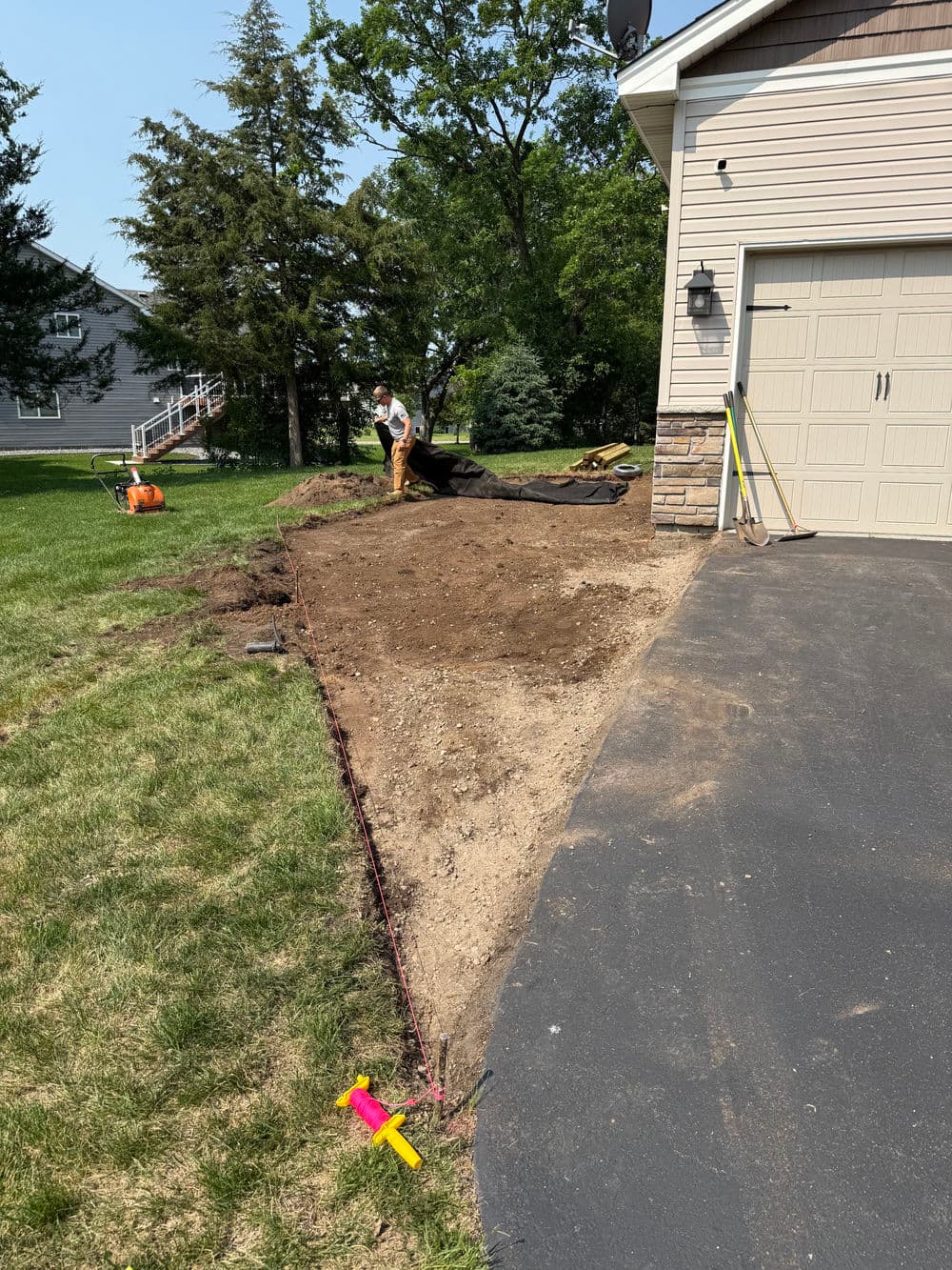 Landscaping project: worker preparing soil for garden bed beside driveway.