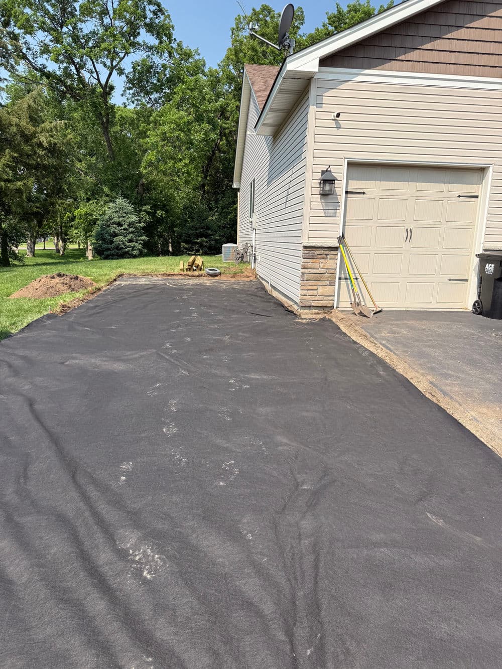 Newly prepared landscape area with black landscaping fabric beside a residential garage.