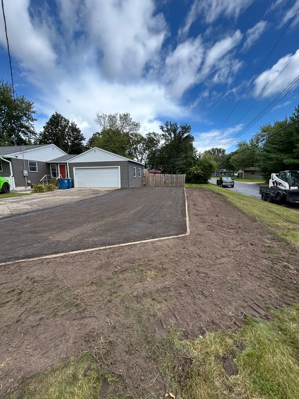 Newly prepared gravel driveway beside house under a clear blue sky with clouds.
