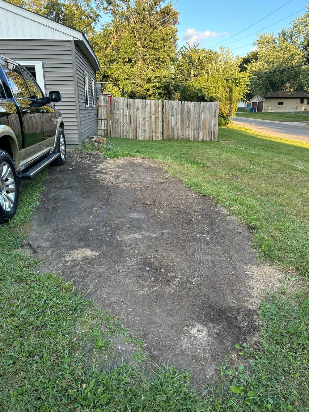 Grassy area next to a house with gravel patch and fence, ideal for landscaping ideas.