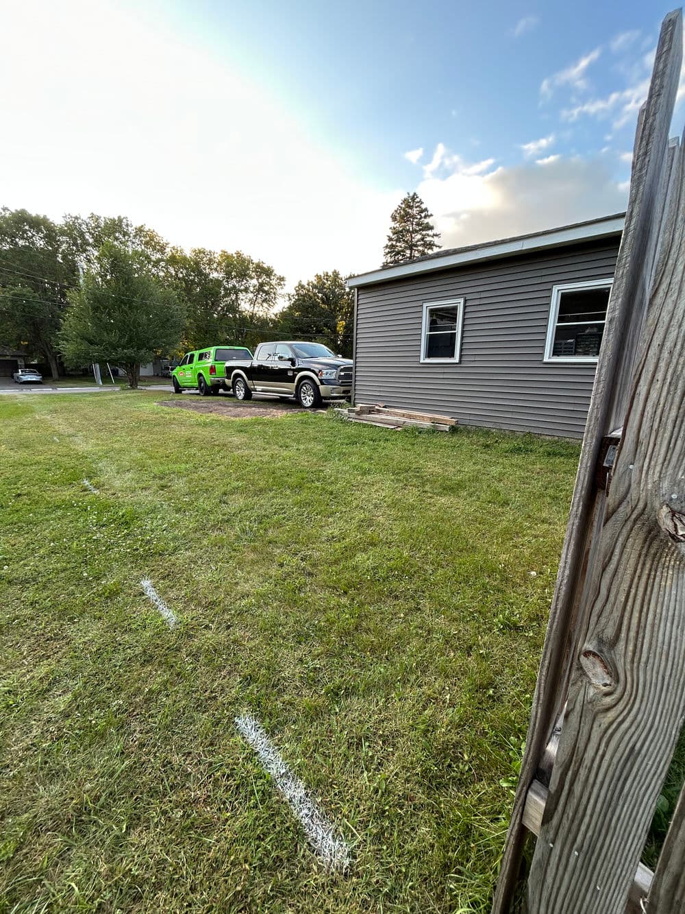 Green vehicle parked beside a house with a grassy yard in the foreground.
