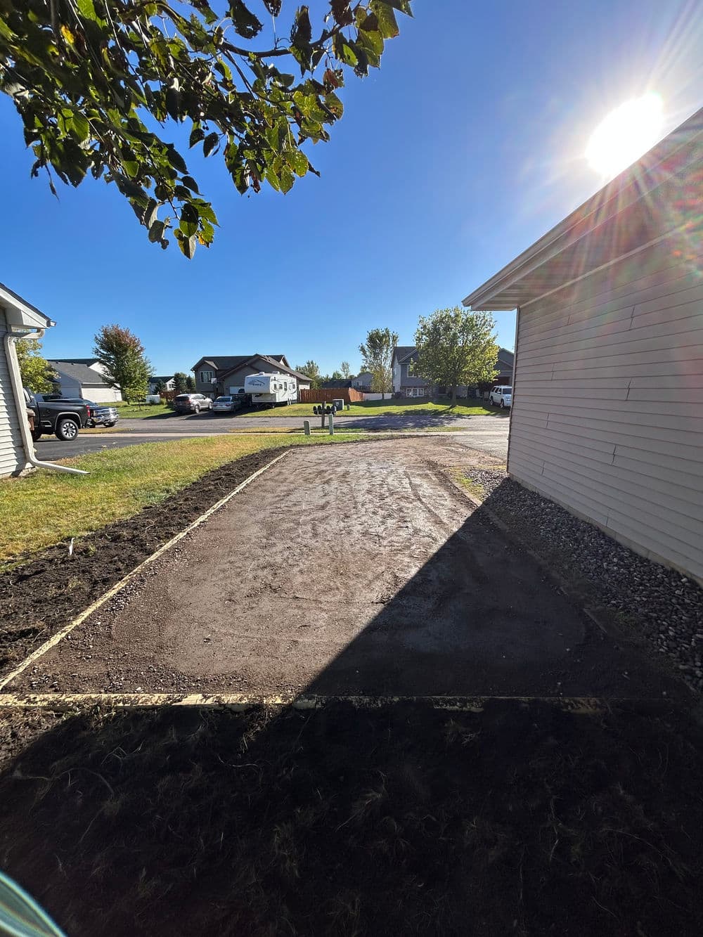 Clear residential area ready for landscaping, featuring sunlit backyard and houses in background.