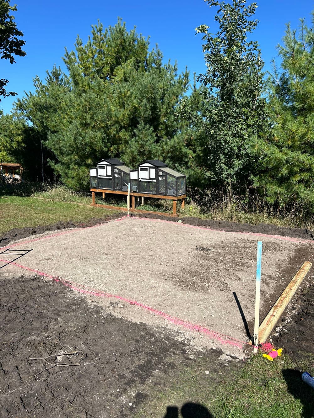 Construction site with gravel base, marked perimeter, and two animal enclosures in background.