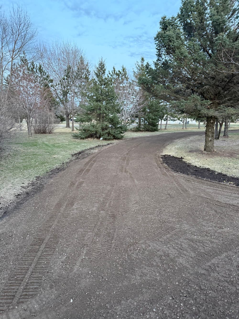 Dirt path winding through a park with green grass and trees on a cloudy day.