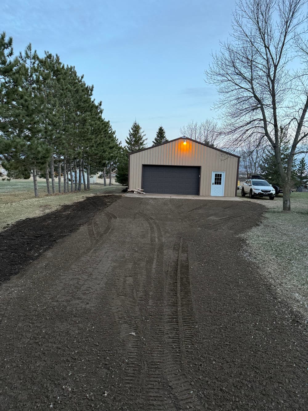 Newly built garage on a gravel driveway surrounded by trees and grassy landscape.