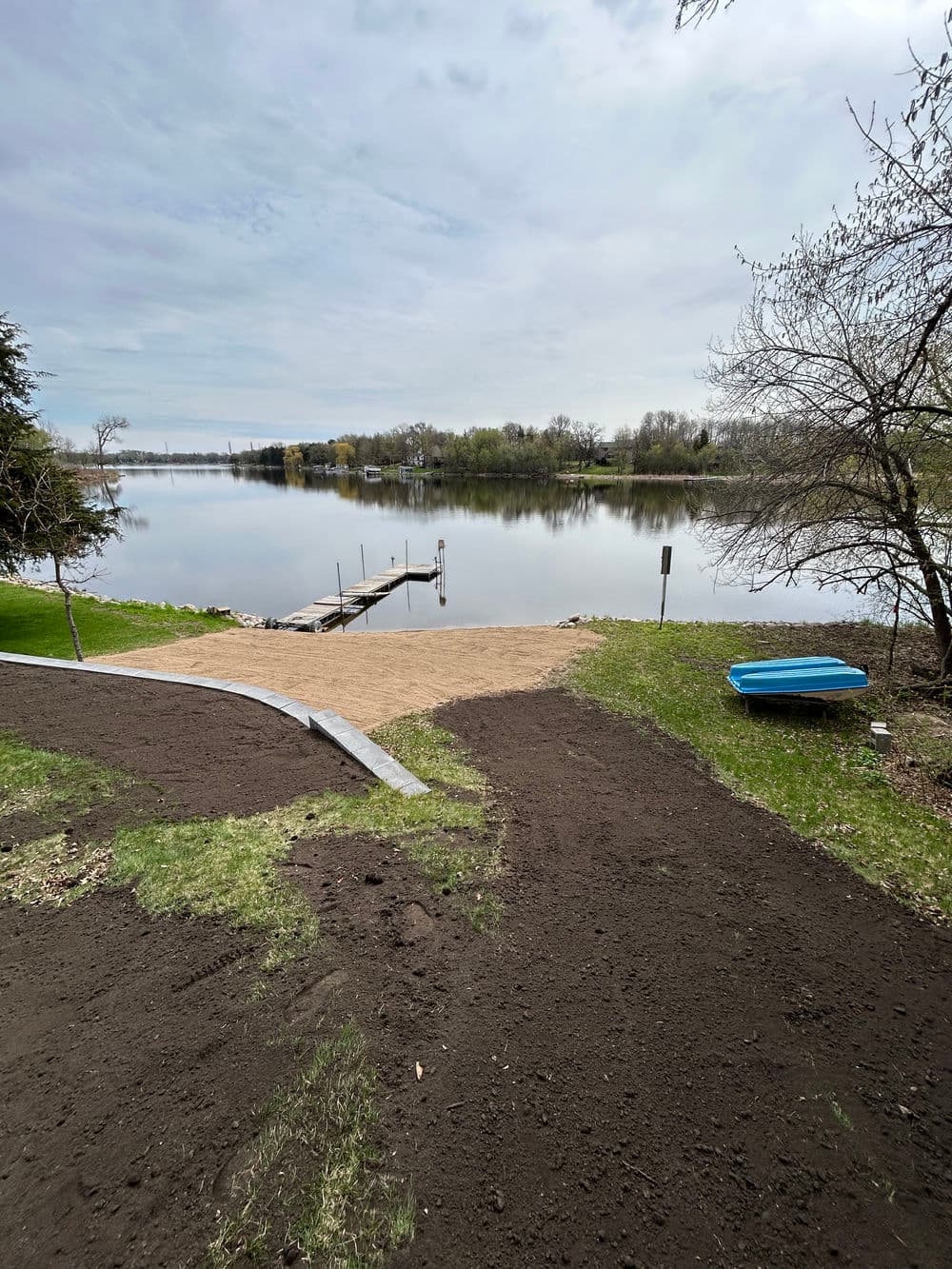 Scenic view of a lake with a sandy shoreline and wooden dock on a cloudy day.