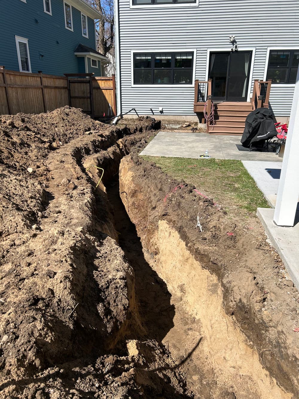 Excavation trench for landscaping behind a house, showing dirt and foundation area.